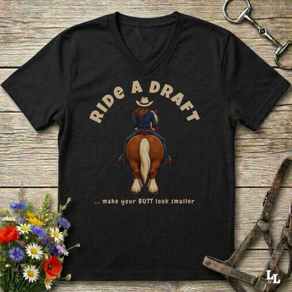 A black V-neck t-shirt laid flat on a rustic wooden surface, featuring a graphic of a cowboy riding a brown horse with the text 'RIDE A DRAFT .