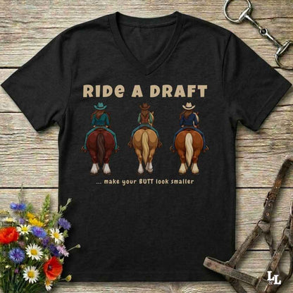 A black V-neck t-shirt laid flat on a rustic wooden surface, featuring a graphic of three cowboys riding horses with the text 'RIDE A DRAFT .