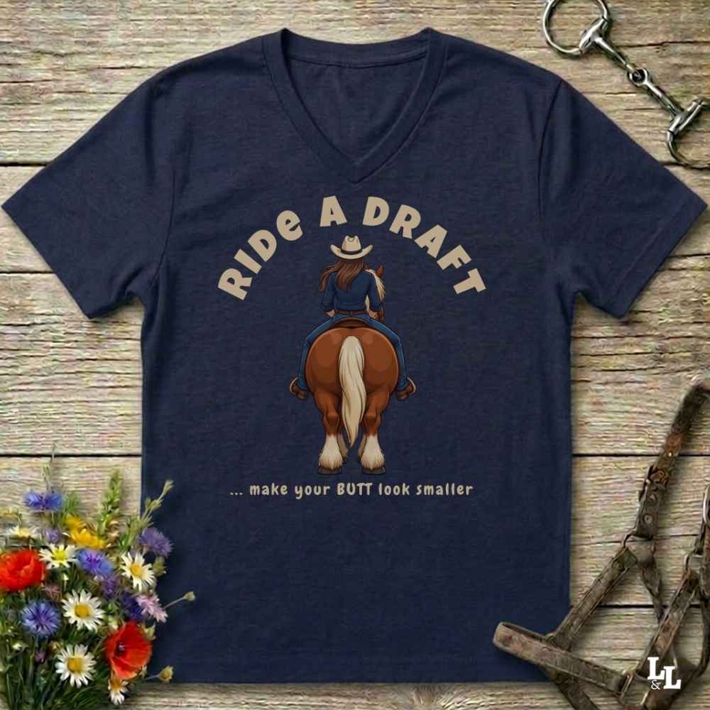 A navy blue V-neck t-shirt laid flat on a rustic wooden surface, featuring a graphic of a cowboy riding a brown horse with the text 'RIDE A DRAFT .
