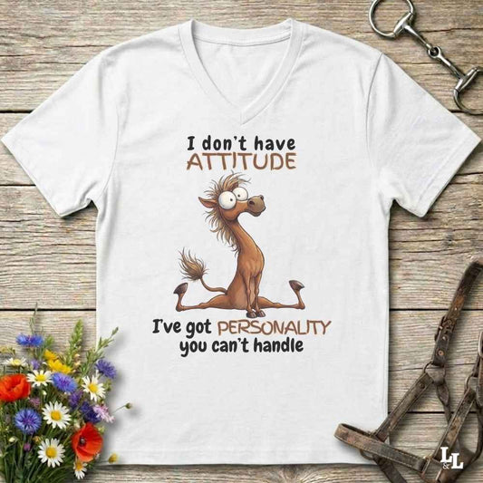 A white V-neck t-shirt with a humorous cartoon horse graphic and text, displayed on a rustic wooden background with equestrian accessories and flowers.