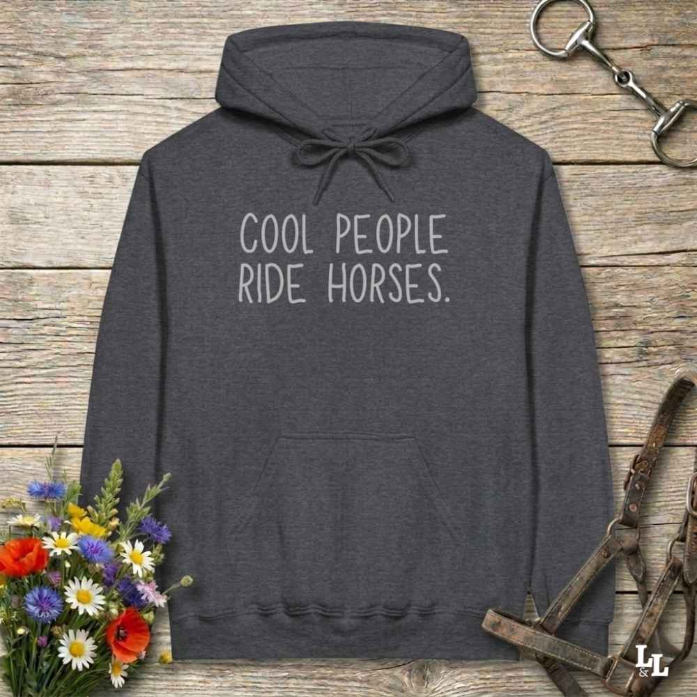 Dark gray hoodie with 'If it involves trail riding, count me in' text on a wooden surface with floral and equestrian elements.