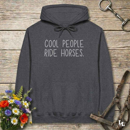 Dark gray hoodie with 'If it involves trail riding, count me in' text on a wooden surface with floral and equestrian elements.