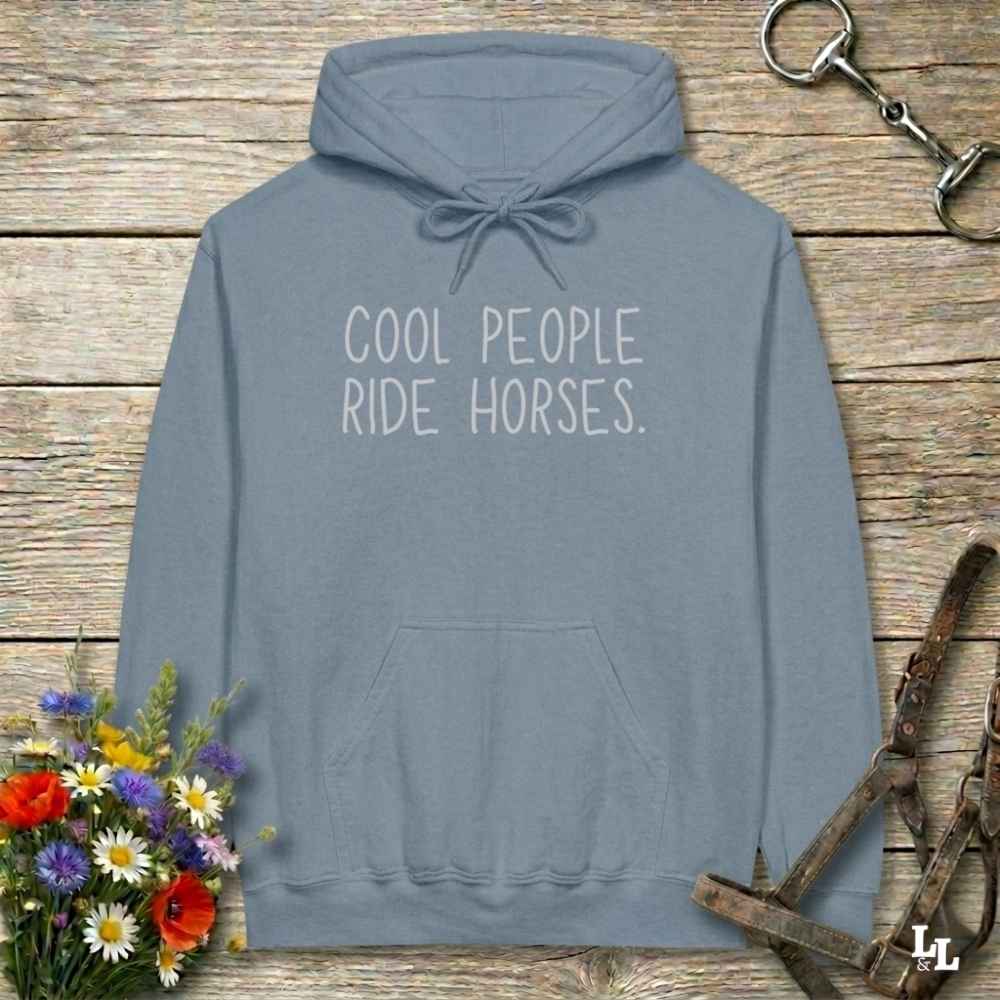 Gray hoodie with 'tremendous horse girl energy believe me' text on a wooden surface with floral and equestrian accessories.