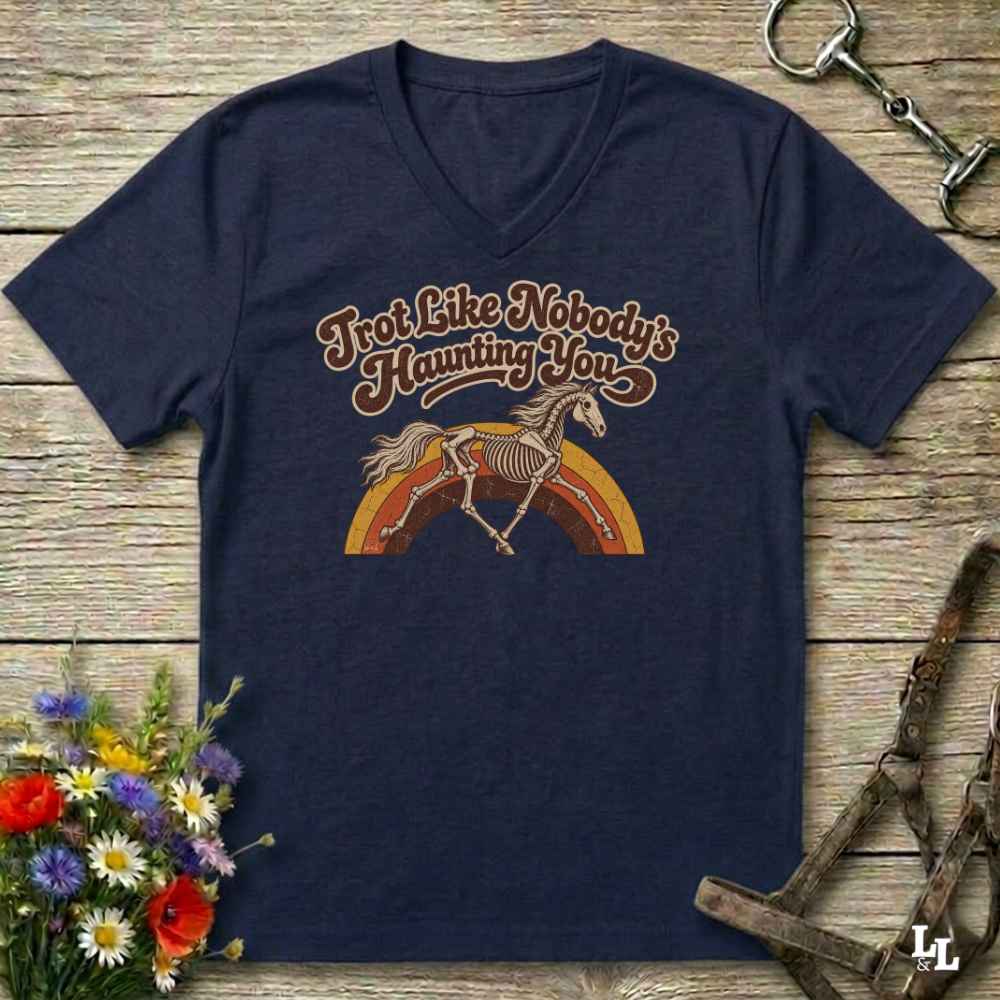 A navy blue V-neck t-shirt with a retro graphic of a horse skeleton running over a rainbow, with the text 'I'm Not Like Nobody's Hamming You'. The shirt is displayed flat on a rustic wooden background with equestrian accessories and flowers.