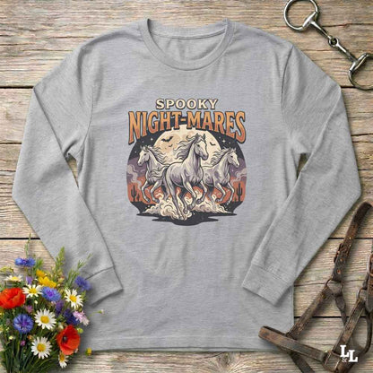 A light gray long-sleeve t-shirt with a 'Spooky Night-Mares' graphic print featuring three white horses and orange flames, displayed flat on a rustic wooden background with decorative floral and leather props.