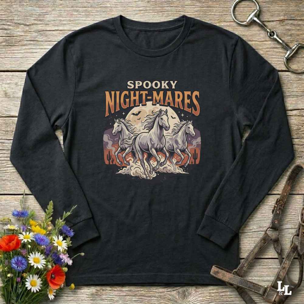 A black long-sleeve t-shirt with a 'Spooky Night-Mares' graphic print, laid flat on a rustic wooden background with equestrian and floral props.