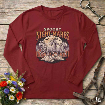 A long-sleeve crewneck t-shirt in maroon red, laid flat on a rustic wooden surface. The shirt features a graphic print of three white horses running in front of a full moon with the text 'SPOOKY NIGHT-MARES'.
