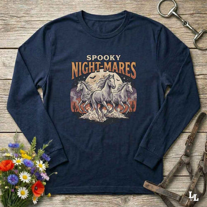 A navy blue long-sleeve t-shirt with a 'Spooky Night-Mares' graphic featuring three white horses and orange flames, laid flat on a rustic wooden background with decorative flowers and horse tack.