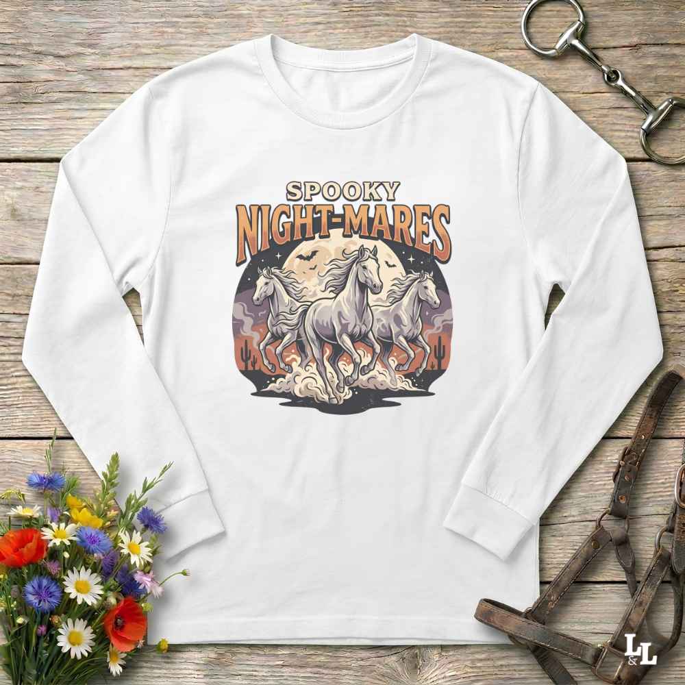 A white long-sleeve t-shirt with a 'Spooky Night-Mares' graphic print, laid flat on a rustic wooden background with equestrian and floral props.