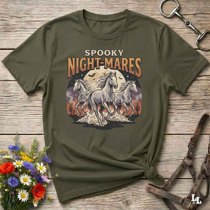 An olive green graphic t-shirt laid flat on a rustic wooden surface, styled with a bouquet of flowers, a horse bit, and a leather halter. The t-shirt features a graphic print of three white horses running in front of a full moon with the text 'SPOOKY NIGHT-MARES'.