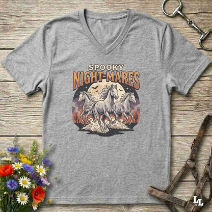 A heather gray V-neck t-shirt with a 'Spooky Night-Mares' graphic print featuring three white horses in front of a full moon. The shirt is displayed flat on a rustic wooden background with decorative equestrian and floral props.