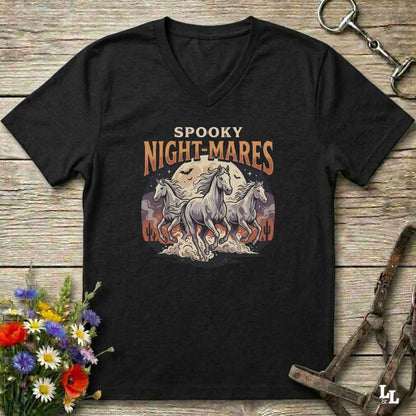 A black V-neck t-shirt with a 'Spooky Night-Mares' graphic featuring three white horses and a full moon, displayed on a rustic wooden background with equestrian accessories and flowers.