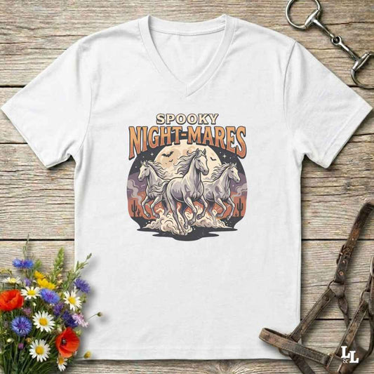 A white V-neck t-shirt with a 'Spooky Night-Mares' graphic print featuring three white horses and a full moon, displayed on a rustic wooden background with decorative flowers and horse tack.
