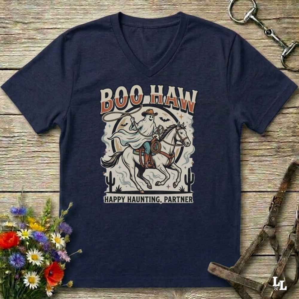 A navy blue V-neck t-shirt with a western-themed 'Boo Haw Happy Haunting, Partner' graphic, laid flat on a rustic wooden background with decorative horse tack and flowers.