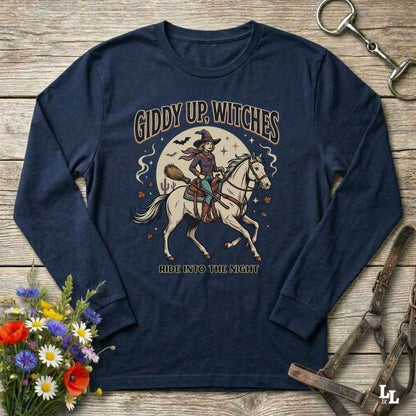 A navy blue long-sleeve t-shirt with a vintage-style graphic of a witch riding a white horse on a wooden background. The graphic features the text 'GIDDY UP, WITCHES' and 'RIDE INTO THE NIGHT' with an illustration of a witch on a broomstick and a moon.