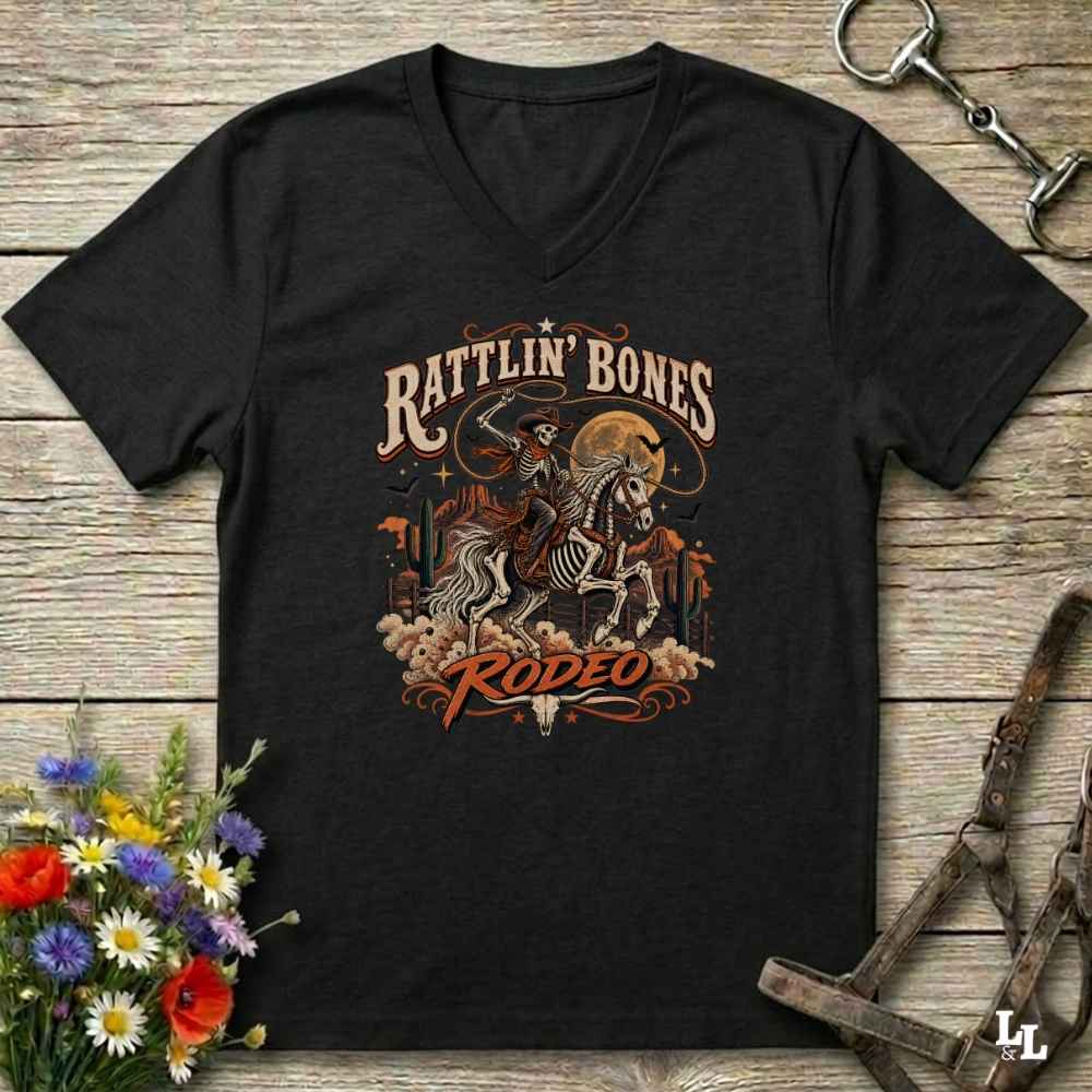 A black  Halloween V-neck t-shirt with a detailed western skeleton cowboy graphic on the chest, styled in a flat-lay on a rustic wooden background with equestrian and floral props.