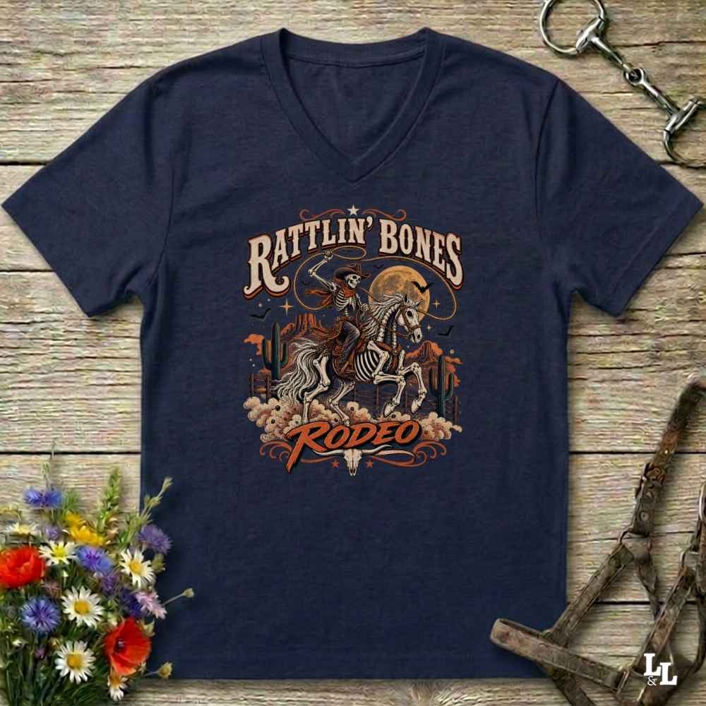 A navy blue Halloween V-neck t-shirt with a detailed western skeleton cowboy graphic on the chest, styled in a flat-lay on a rustic wooden background with equestrian and floral props.