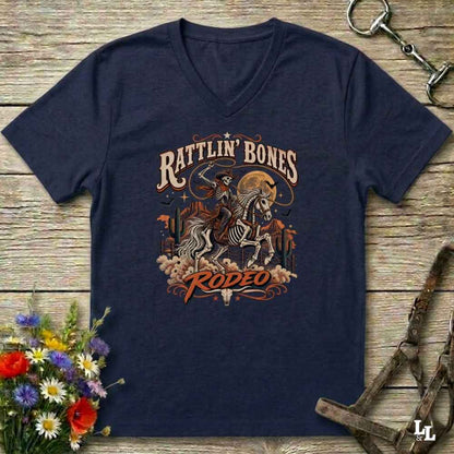 A navy blue Halloween V-neck t-shirt with a detailed western skeleton cowboy graphic on the chest, styled in a flat-lay on a rustic wooden background with equestrian and floral props.