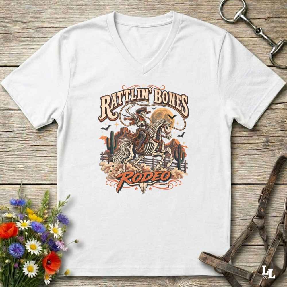 A white Halloween V-neck t-shirt with a detailed western skeleton cowboy graphic on the chest, styled in a flat-lay on a rustic wooden background with equestrian and floral props.