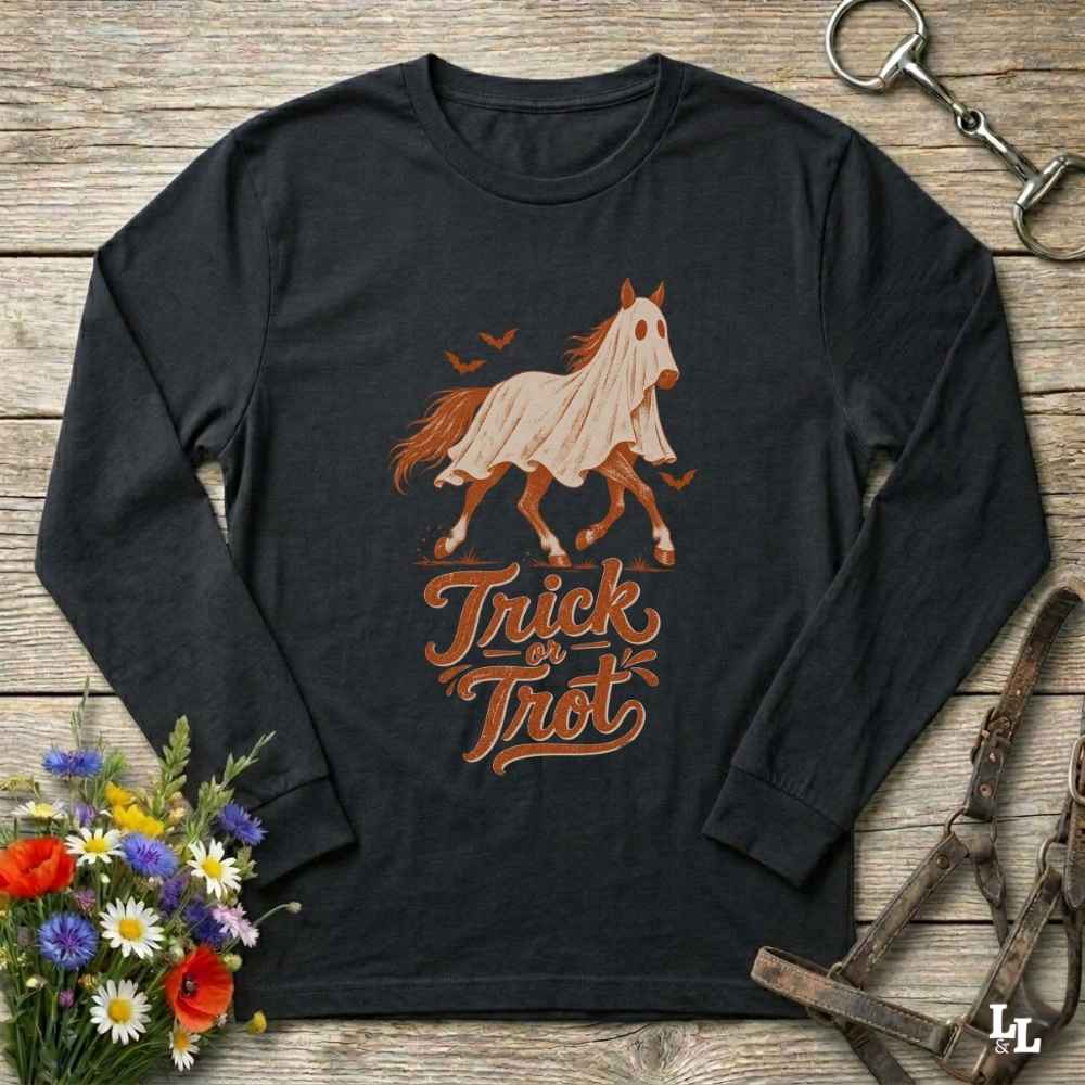 A black long-sleeve t-shirt with a 'Trick or Treat' ghost horse graphic, displayed in a flat-lay arrangement on a rustic wooden background with equestrian and floral props.
