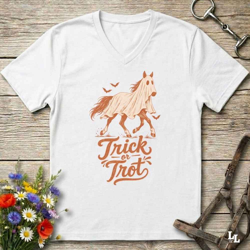 A white V-neck t-shirt with a graphic of a ghostly horse and the words 'Trick or Treat' in orange, laid flat on a rustic wooden background with decorative flowers and horse tack.
