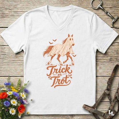 A white V-neck t-shirt with a graphic of a ghostly horse and the words 'Trick or Treat' in orange, laid flat on a rustic wooden background with decorative flowers and horse tack.