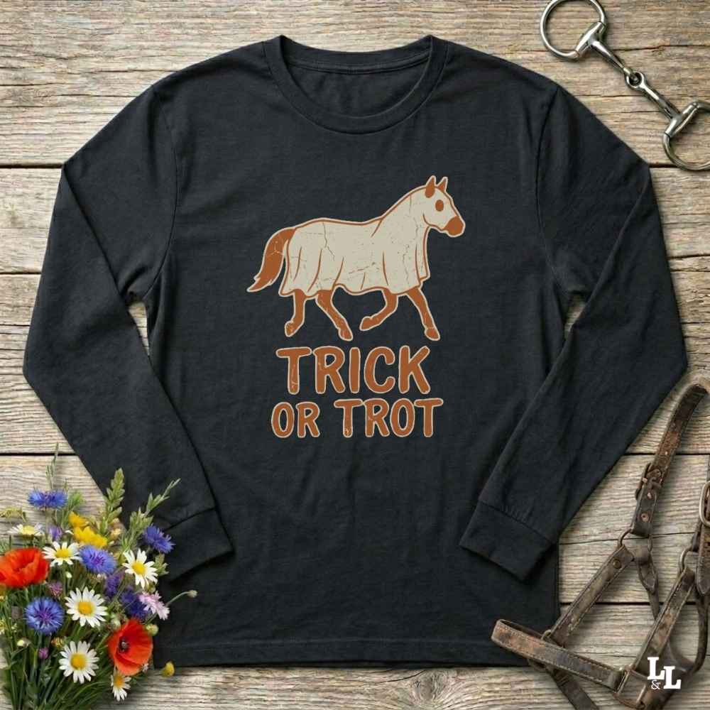 A black long-sleeve t-shirt with a graphic of a horse and the text 'TRICK OR TROT' in brown, styled on a rustic wooden background with equestrian accessories and flowers.