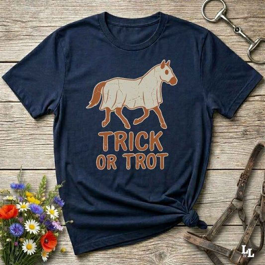 A navy blue graphic t-shirt featuring a cream-colored horse illustration and the words 'TRICK OR TROT' in brown, styled on a rustic wooden background with equestrian accessories and flowers.