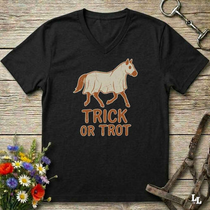 A black V-neck t-shirt with a graphic of a horse and the text 'TRICK OR TROT' in brown, laid flat on a rustic wooden background with equestrian accessories and flowers.