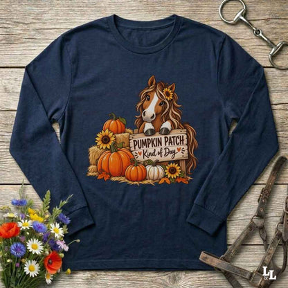 A navy blue long-sleeve t-shirt with a graphic of a brown horse surrounded by pumpkins, sunflowers, and a sign that reads 'Pumpkin Patch Kind of Dog'. The shirt is displayed in a flat-lay arrangement on a rustic wooden background, styled with a bouquet of flowers, a horse bit, and a leather bridle.