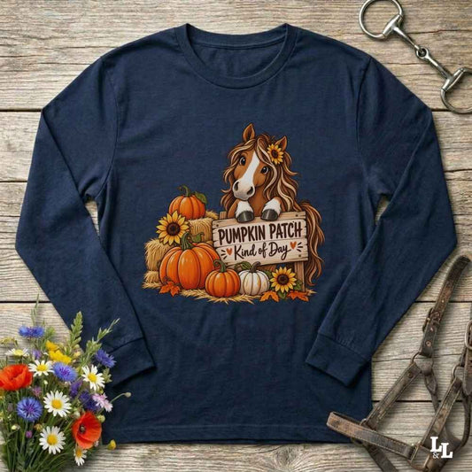 A navy blue long-sleeve t-shirt with a graphic of a brown horse surrounded by pumpkins, sunflowers, and a sign that reads 'Pumpkin Patch Kind of Dog'. The shirt is displayed in a flat-lay arrangement on a rustic wooden background, styled with a bouquet of flowers, a horse bit, and a leather bridle.