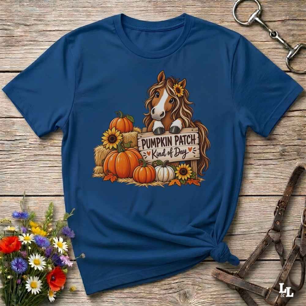 A navy blue short-sleeve t-shirt with a graphic of a brown horse and pumpkins on a wooden background, styled with equestrian accessories and flowers.