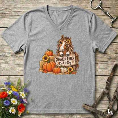A greV-neck t-shirt laid flat on a rustic wooden surface, featuring a graphic of a brown horse behind a sign that reads 'PUMPKIN PATCH Kind of Boy' surrounded by pumpkins, sunflowers, and hay bales. The shirt is styled with horse tack and flowers around it. 