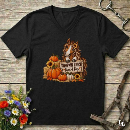 A black V-neck t-shirt laid flat on a rustic wooden surface, featuring a graphic of a brown horse behind a sign that reads 'PUMPKIN PATCH Kind of Boy' surrounded by pumpkins, sunflowers, and hay bales. The shirt is styled with horse tack and flowers around it.