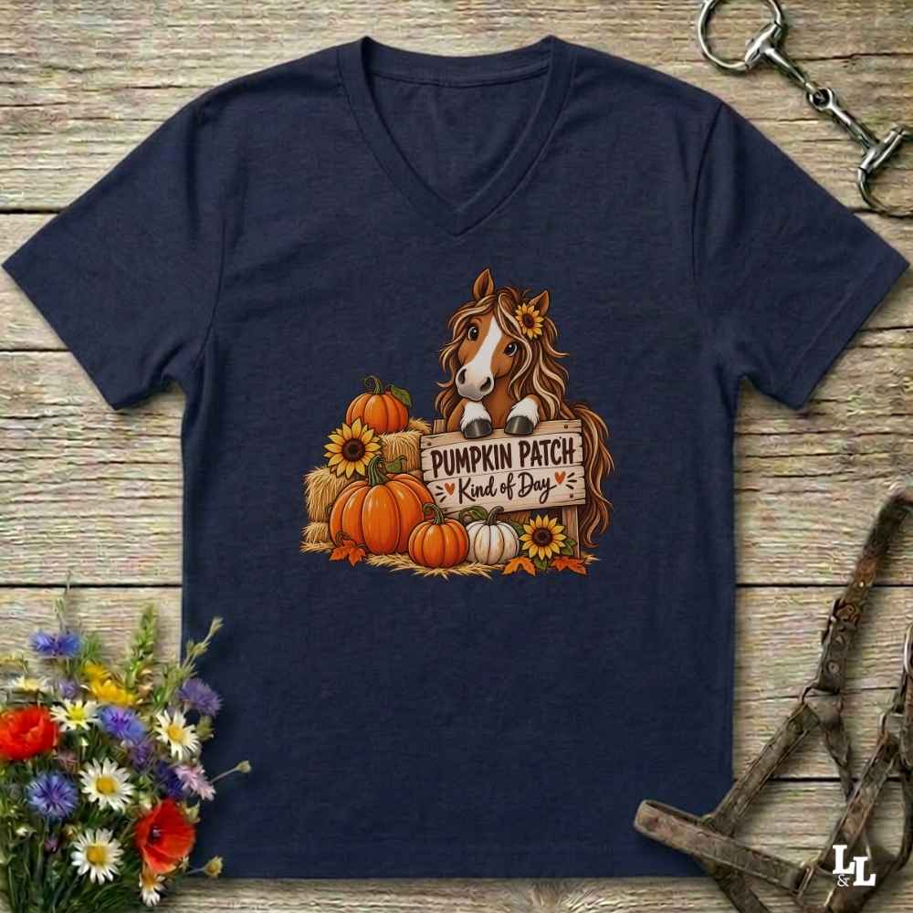 A navy blue V-neck t-shirt laid flat on a rustic wooden surface, featuring a graphic of a brown horse behind a sign that reads 'PUMPKIN PATCH Kind of Boy' surrounded by pumpkins, sunflowers, and hay bales. The shirt is styled with horse tack and flowers around it.