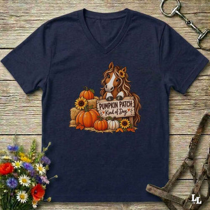 A navy blue V-neck t-shirt laid flat on a rustic wooden surface, featuring a graphic of a brown horse behind a sign that reads 'PUMPKIN PATCH Kind of Boy' surrounded by pumpkins, sunflowers, and hay bales. The shirt is styled with horse tack and flowers around it.