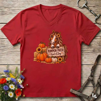 A red V-neck t-shirt laid flat on a rustic wooden surface, featuring a graphic of a brown horse behind a sign that reads 'PUMPKIN PATCH Kind of Boy' surrounded by pumpkins, sunflowers, and hay bales. The shirt is styled with horse tack and flowers around it.