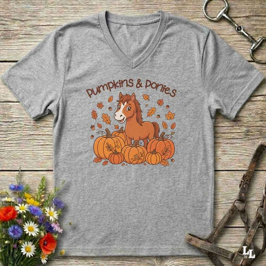 A heather gray V-neck t-shirt with a 'Pumpkins & Ponies' graphic, laid flat on a rustic wooden background with decorative autumn props.