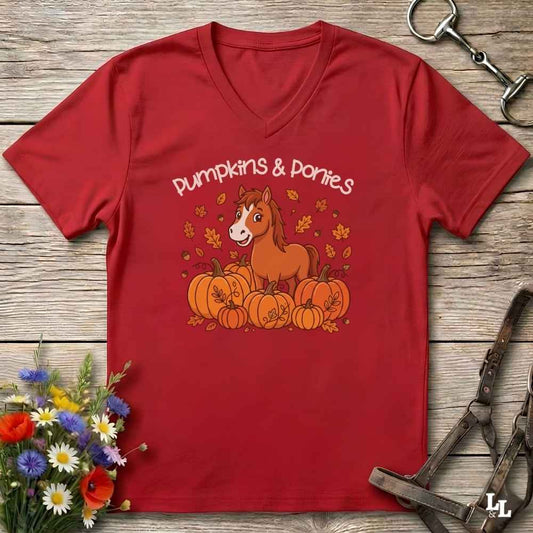A red V-neck t-shirt with a 'Pumpkins & Ponies' graphic, laid flat on a rustic wooden background with decorative autumn props.