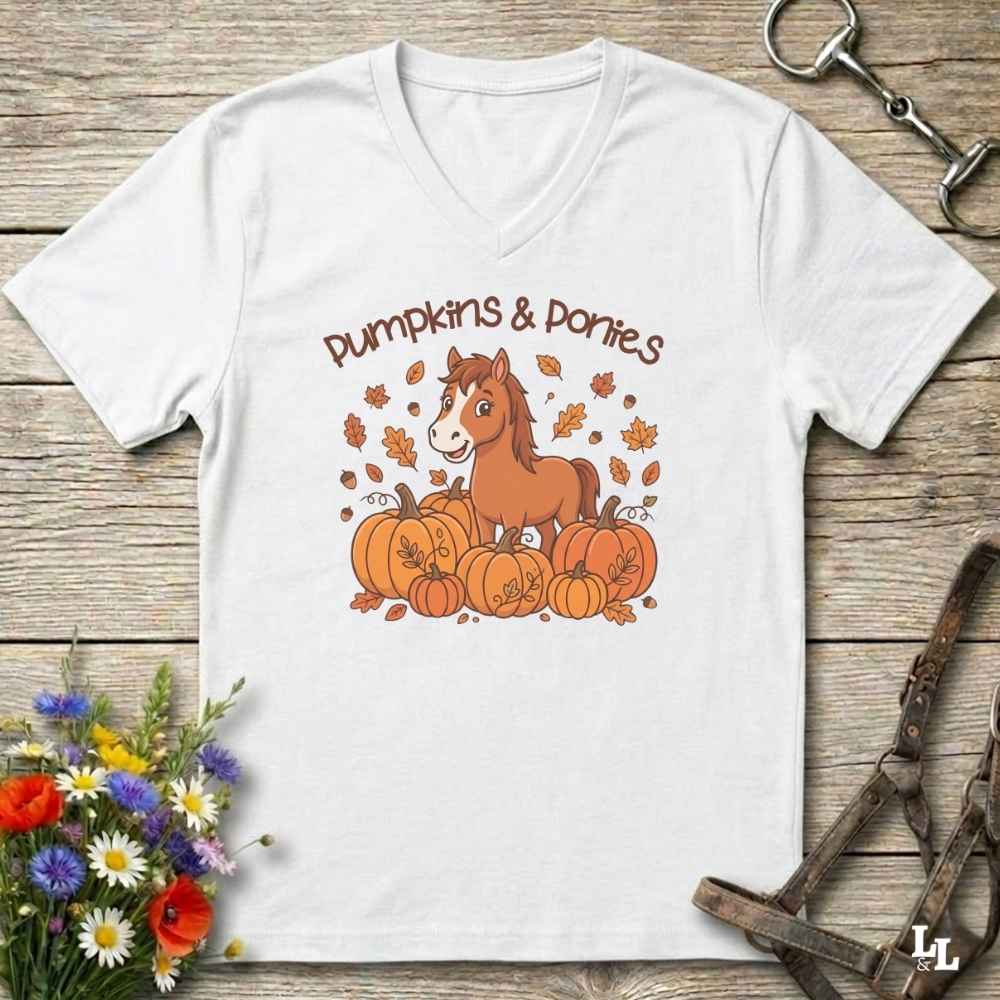 A white V-neck t-shirt with a cartoon graphic of a brown horse standing on a pile of orange pumpkins with the text 'Pumpkins & Porties' above it. The shirt is displayed flat on a rustic wooden background with decorative equestrian and floral props.