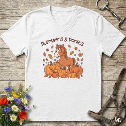 A white V-neck t-shirt with a cartoon graphic of a brown horse standing on a pile of orange pumpkins with the text 'Pumpkins & Porties' above it. The shirt is displayed flat on a rustic wooden background with decorative equestrian and floral props.