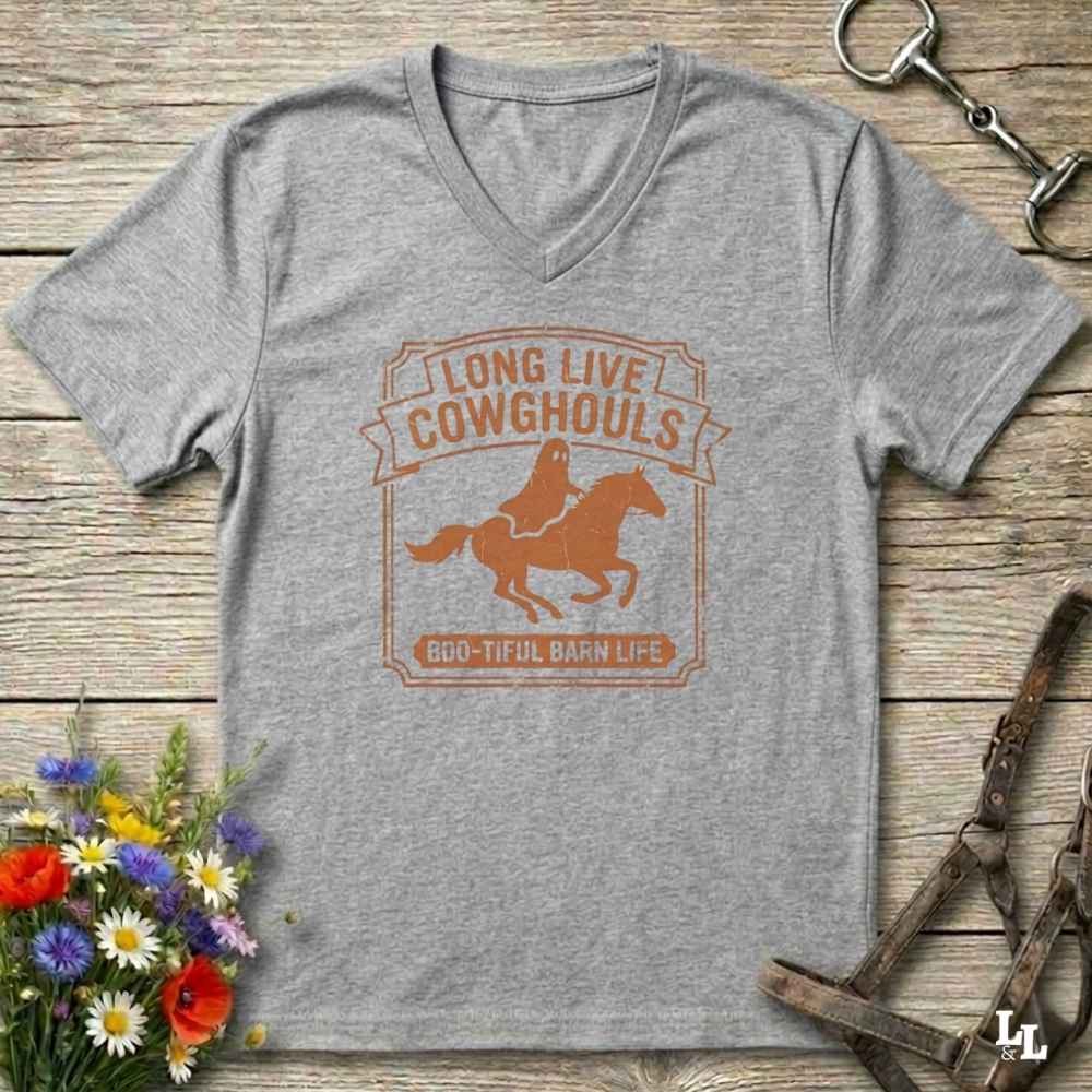 A heather gray V-neck t-shirt with a distressed brown graphic reading 'LONG LIVE COWHOULS' and '666-TIFUL BARN LIFE' around an illustration of a cowboy on a horse, laid flat on a rustic wood background with equestrian and floral props.
