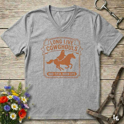 A heather gray V-neck t-shirt with a distressed brown graphic reading 'LONG LIVE COWHOULS' and '666-TIFUL BARN LIFE' around an illustration of a cowboy on a horse, laid flat on a rustic wood background with equestrian and floral props.