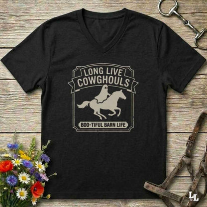 A black V-neck t-shirt with a distressed white graphic reading 'LONG LIVE COWHOOLS' and 'BOO-TIFUL BARN LIFE' around a ghost riding a horse silhouette, displayed on a rustic wooden background with equestrian accessories and flowers.