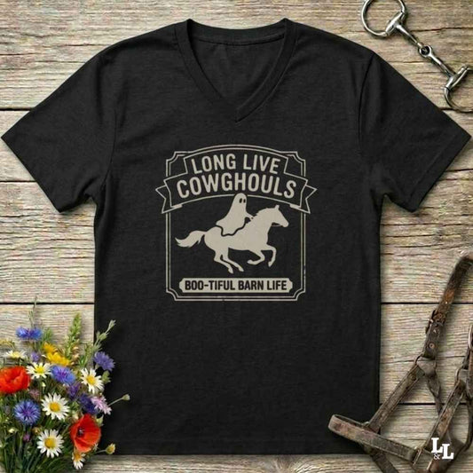 A black V-neck t-shirt with a distressed white graphic reading 'LONG LIVE COWHOOLS' and 'BOO-TIFUL BARN LIFE' around a ghost riding a horse silhouette, displayed on a rustic wooden background with equestrian accessories and flowers.