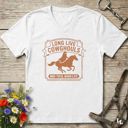 A white V-neck t-shirt laid flat on a rustic wooden surface, featuring a brown graphic of a cowboy riding a horse with the text 'LONG LIVE COWHOULS' and '800-TIFUL BARN LIFE'. The shirt is styled with equestrian and floral props.