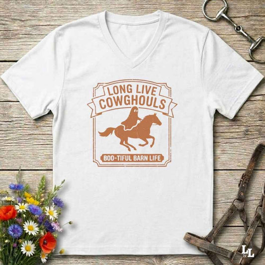 A white V-neck t-shirt laid flat on a rustic wooden surface, featuring a brown graphic of a cowboy riding a horse with the text 'LONG LIVE COWHOULS' and '800-TIFUL BARN LIFE'. The shirt is styled with equestrian and floral props.