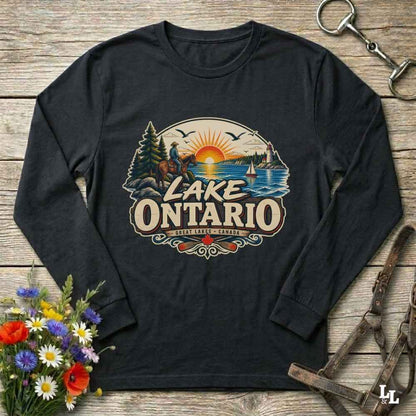 A black long-sleeve t-shirt with a colorful 'Lake Ontario' graphic print, laid flat on a rustic wooden background with decorative flowers and leather tack.