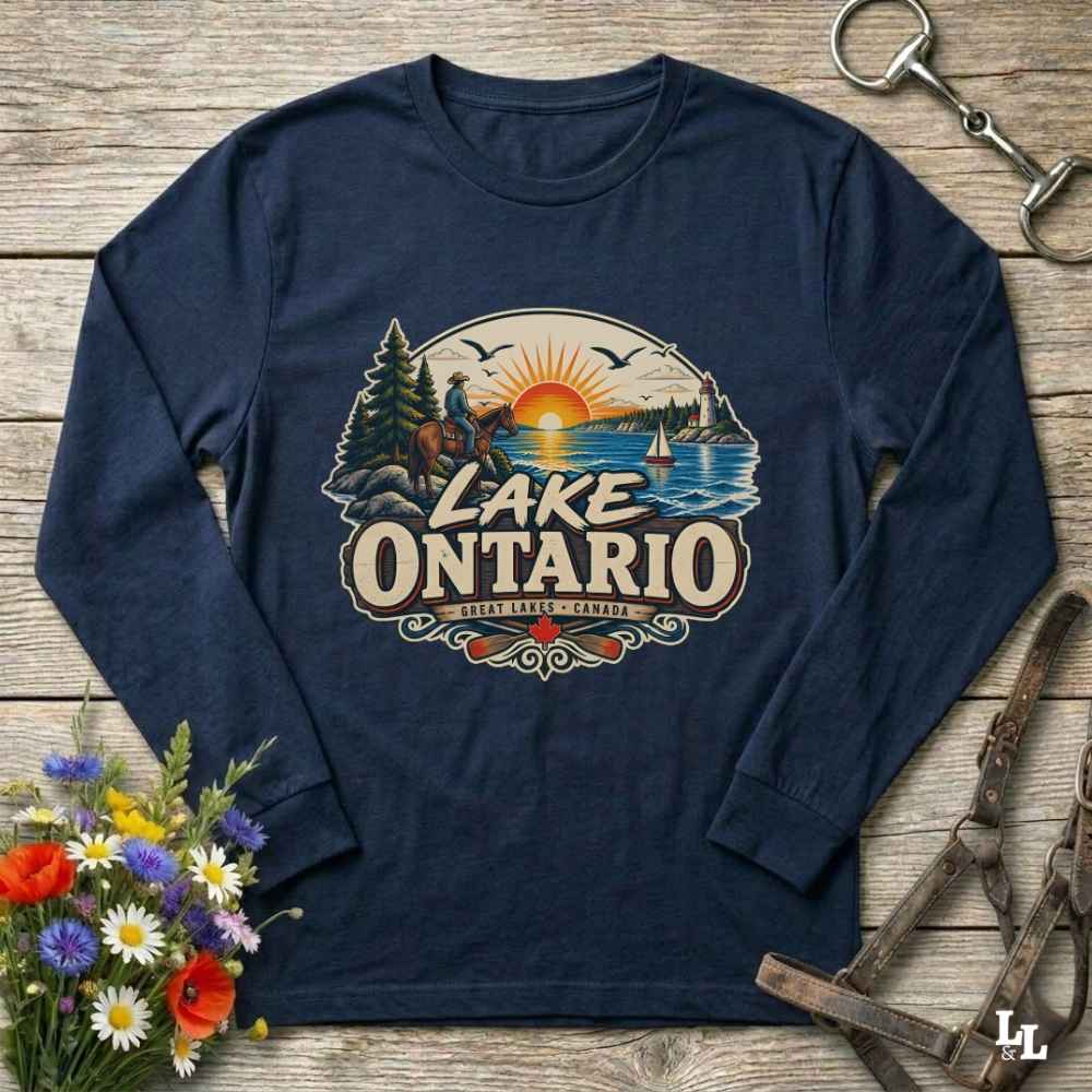 A navy blue long-sleeve t-shirt with a vintage-style 'Lake Ontario' graphic print, laid flat on a rustic wooden background with decorative flowers and equestrian tack.