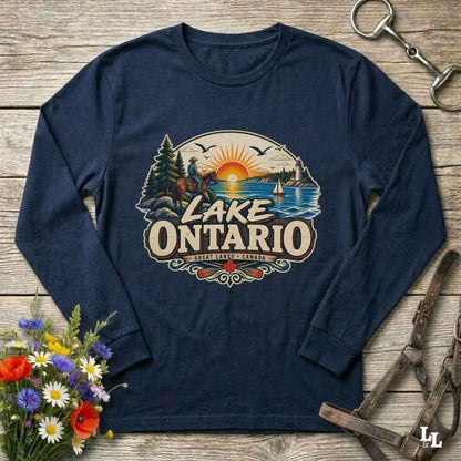 A navy blue long-sleeve t-shirt with a vintage-style 'Lake Ontario' graphic print, laid flat on a rustic wooden background with decorative flowers and equestrian tack.